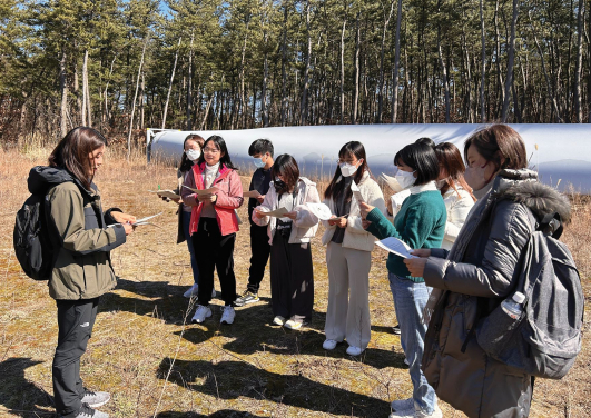 At the Katagami Wind Farm, the project coordinator explains the overview of the Katagami Wind Farm project. Behind the student is the blade of wind turbine.